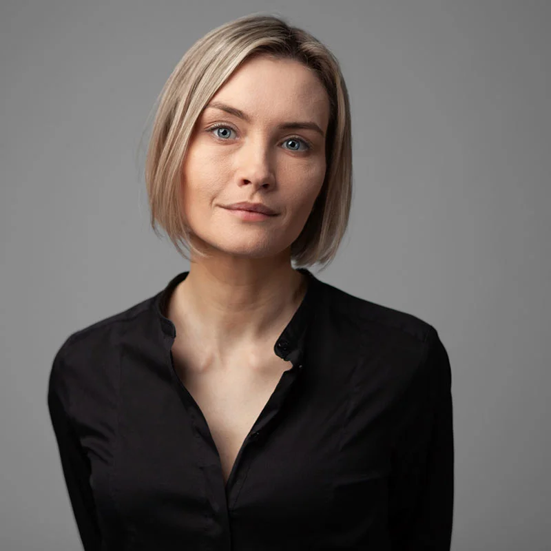 Blonde woman in black top posting with gray background behind her